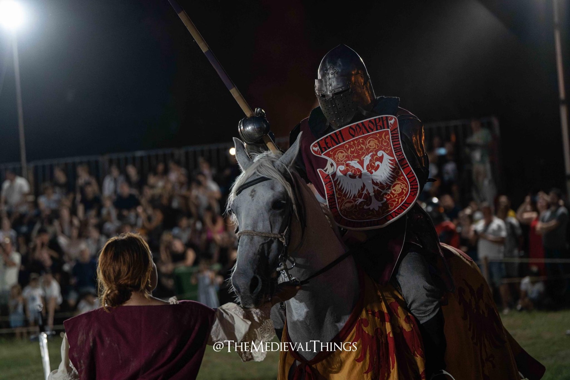 An armoured knight with shield and lance in the lists at a night tournament