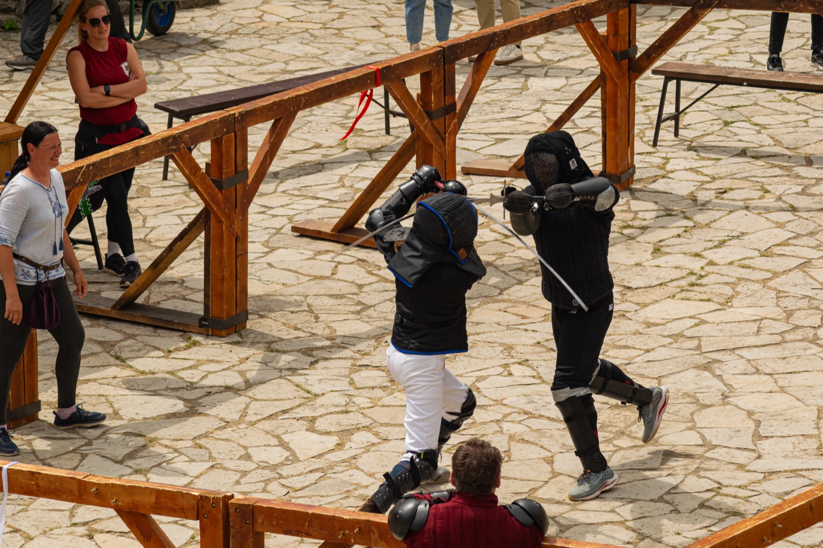 Two fencers crossing swords inside the tournament ring on a stone-paved courtyard, seen from above