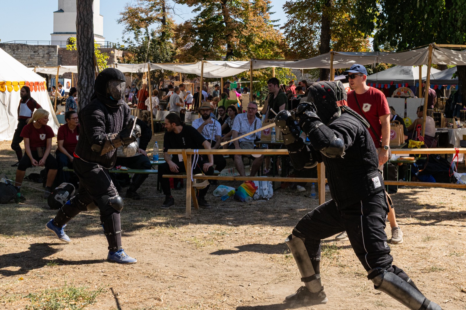 Two fencers squaring off in the arena while festival visitors watch from the rail