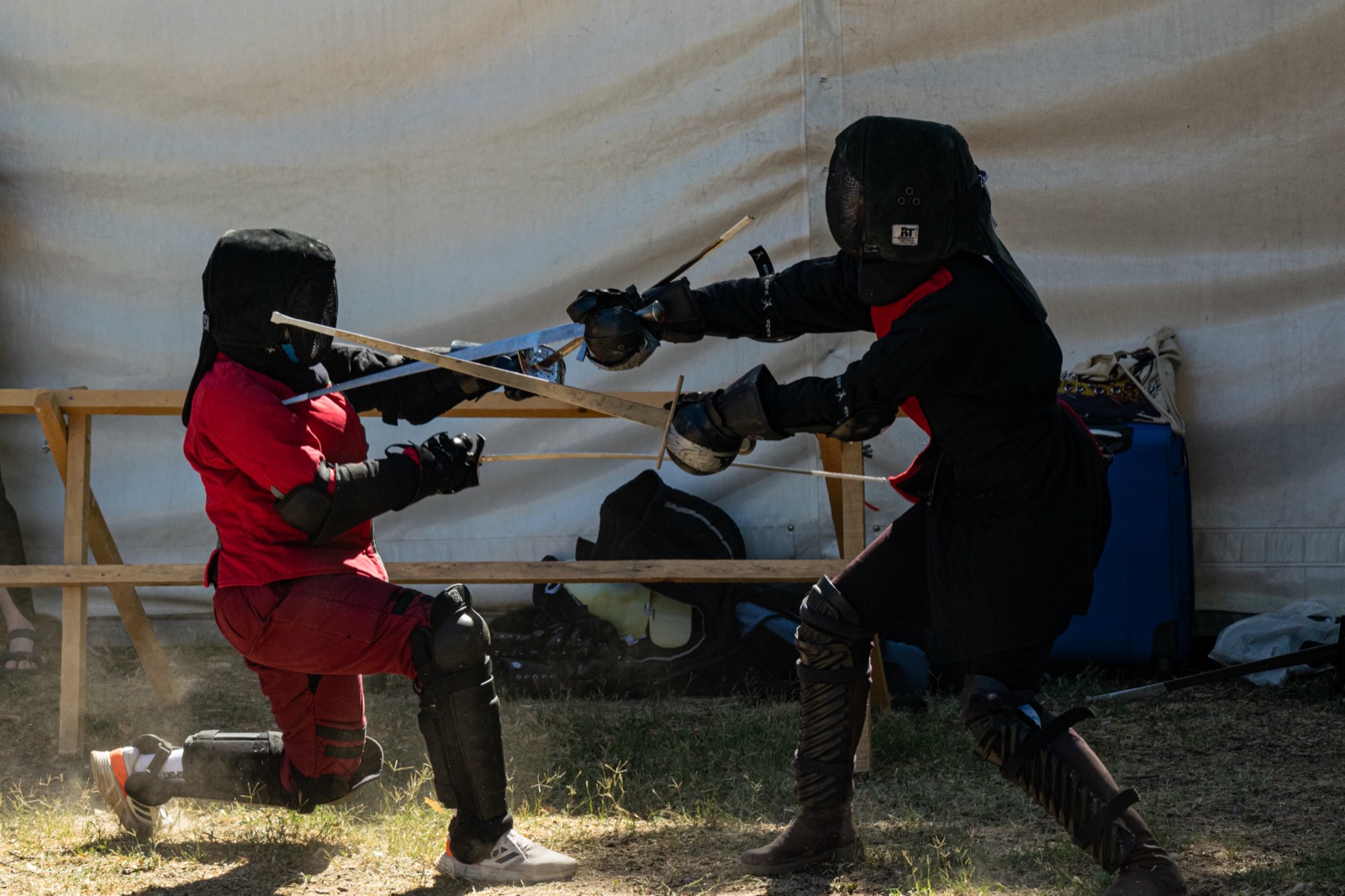A fencer in red and a fencer in black meeting in the bind against a tent wall